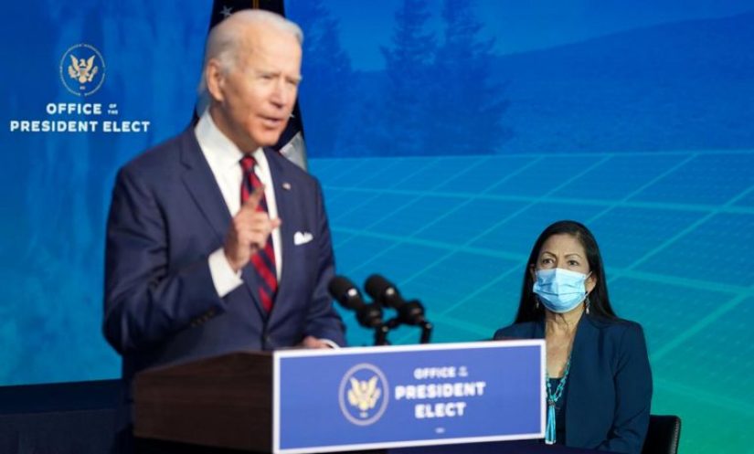 Biden speaking at a podium, women in mask sitting behind.