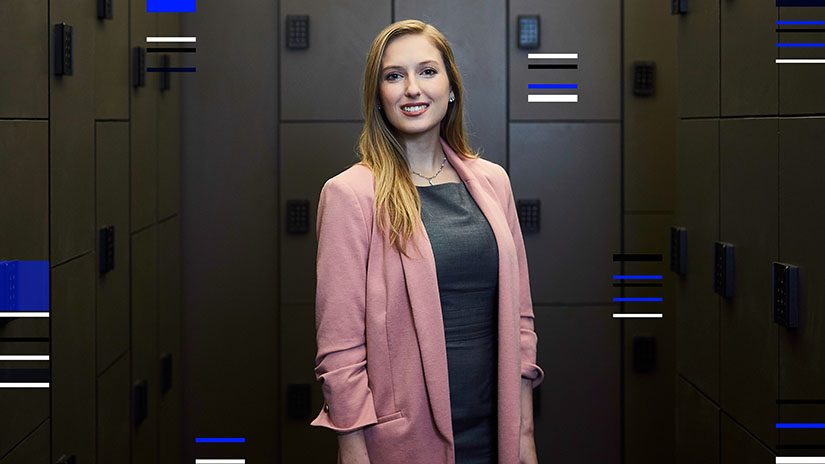 A woman in a pink coat stands in a bank vault. Blue, white and black stripes overlay the edges