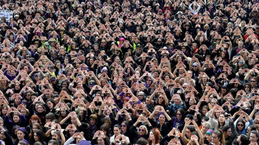 A vast crowd of men and women collectively portraying a triangle sign with their hands
