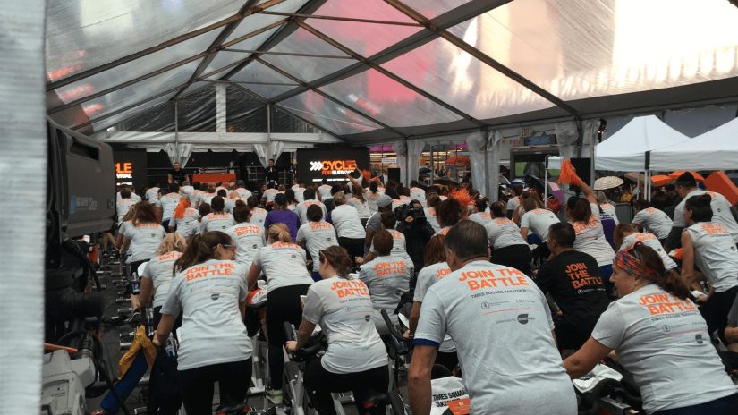 A group of Refinitiv employees cycling in an indoor event and wearing join the battle shirts.
