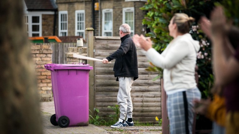 Woman claps whilst man bangs on bin lid with sticks.