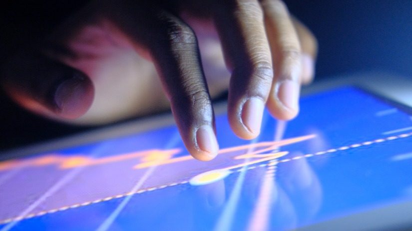 A hand touches a tablet with a line graph displayed