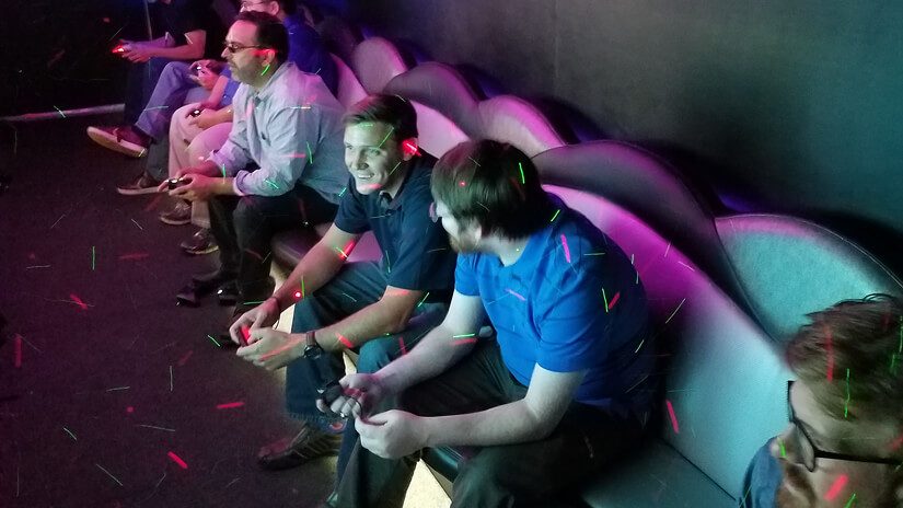 A group of men sit on a bench with video game controllers in their hands